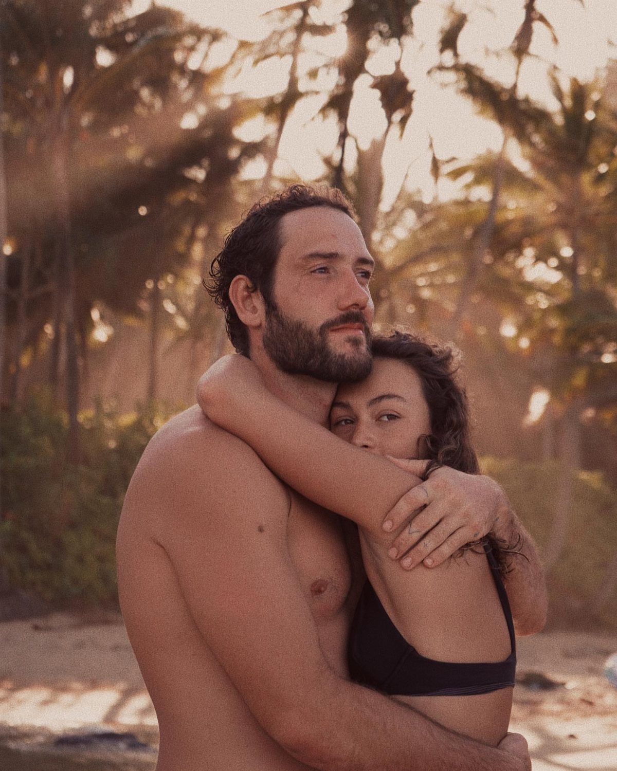 Couple hugging on a beach with the woman embracing the man from behind.