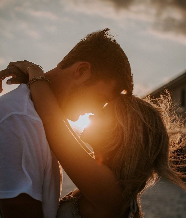 Couple embracing and kissing at sunset with the sun glowing between their faces.