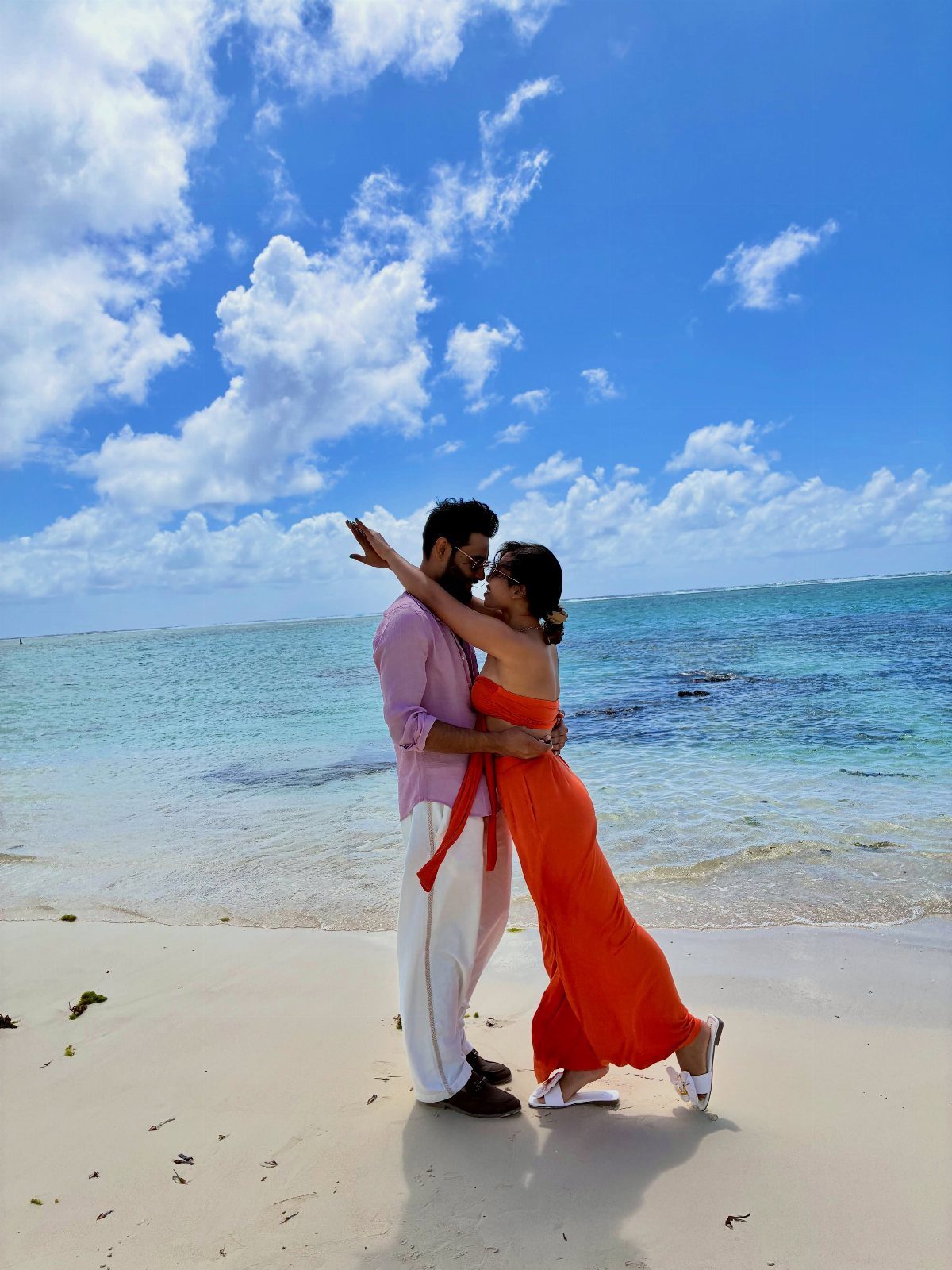 Couple embracing on a white sandy beach with turquoise water and blue sky.