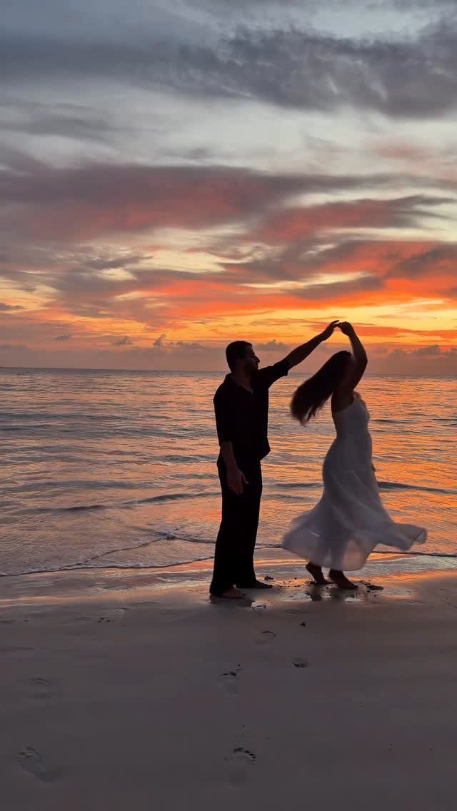 Couple dancing in silhouette on a beach during a vibrant orange sunset.
