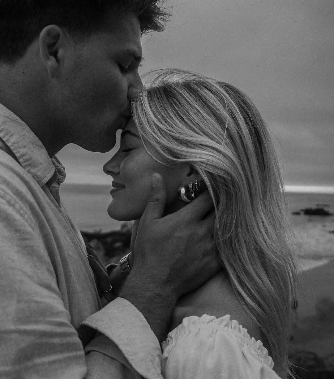 Man kissing a blonde woman on the forehead at a beach