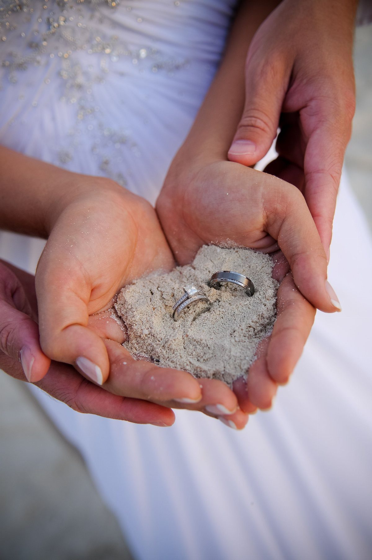 Two wedding rings resting in sand held by a couple's cupped hands