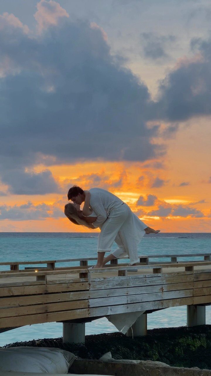 Couple in white dancing on a pier during a vibrant orange sunset beach scene.