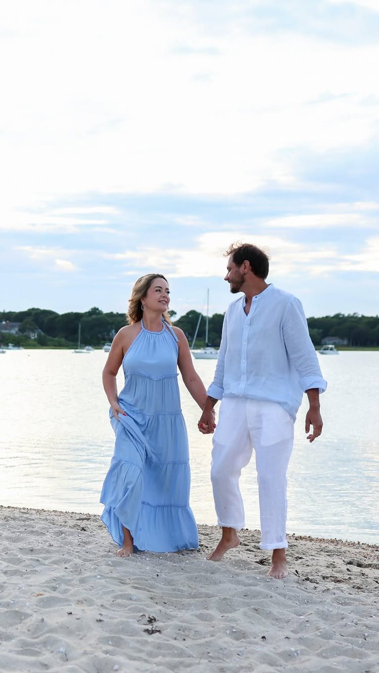 Couple walking hand-in-hand on a sandy beach at dusk by the water
