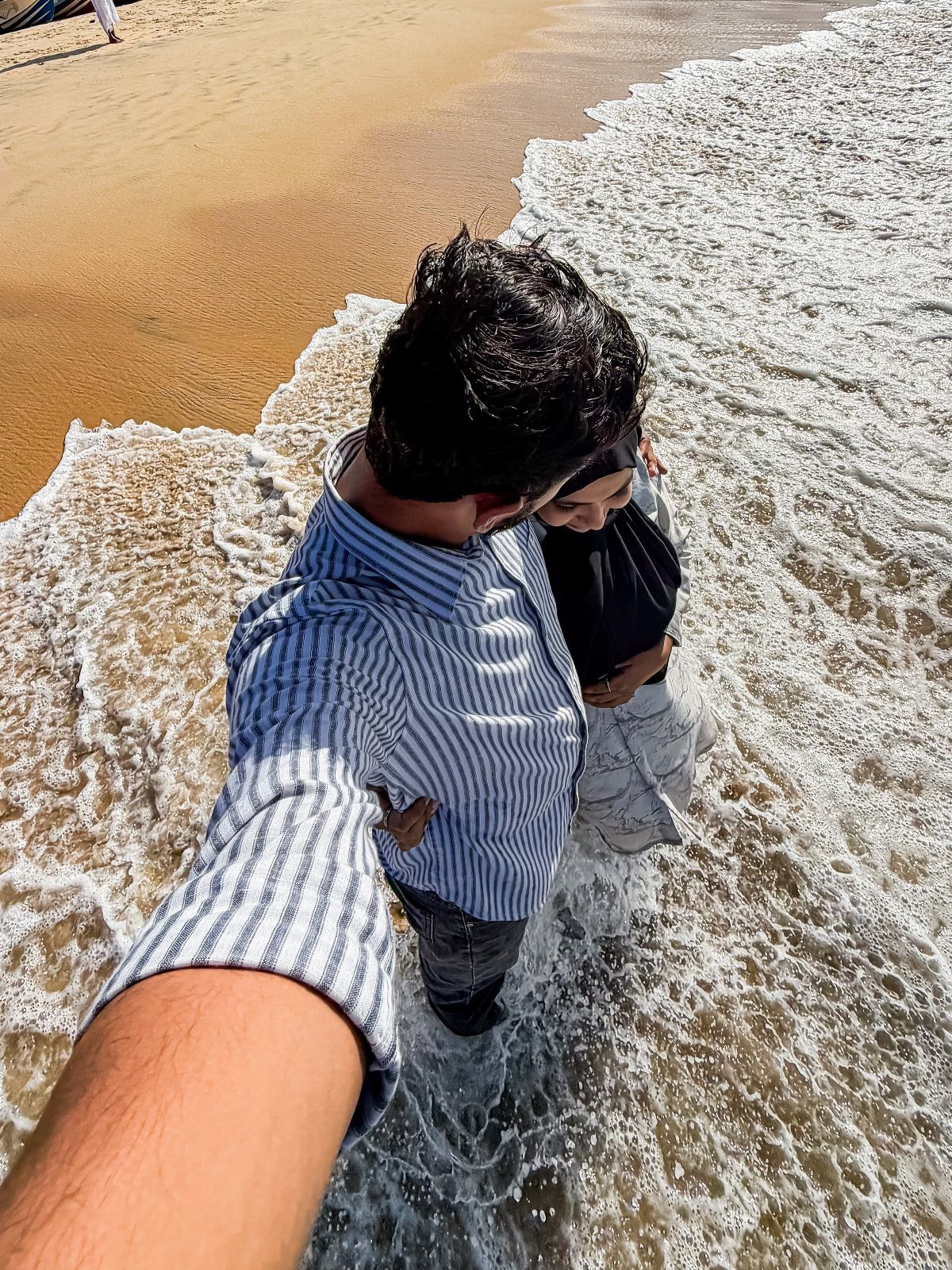 Couple taking a selfie while standing in ocean waves on a sandy beach