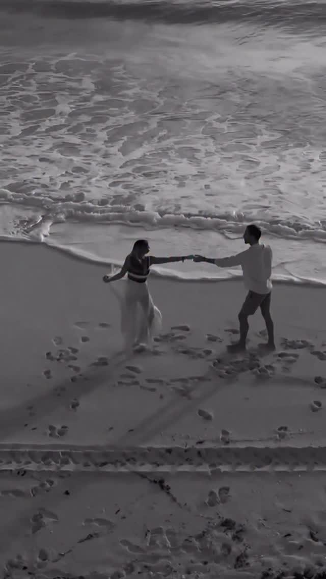 Couple holding hands and dancing on a sandy beach with ocean waves crashing