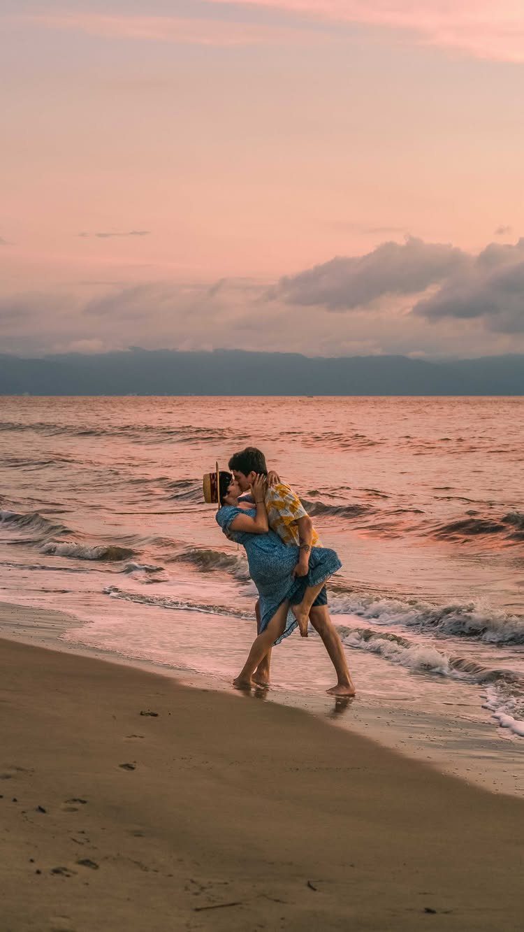 Couple kissing and embracing while standing in shallow ocean waves at sunset beach.