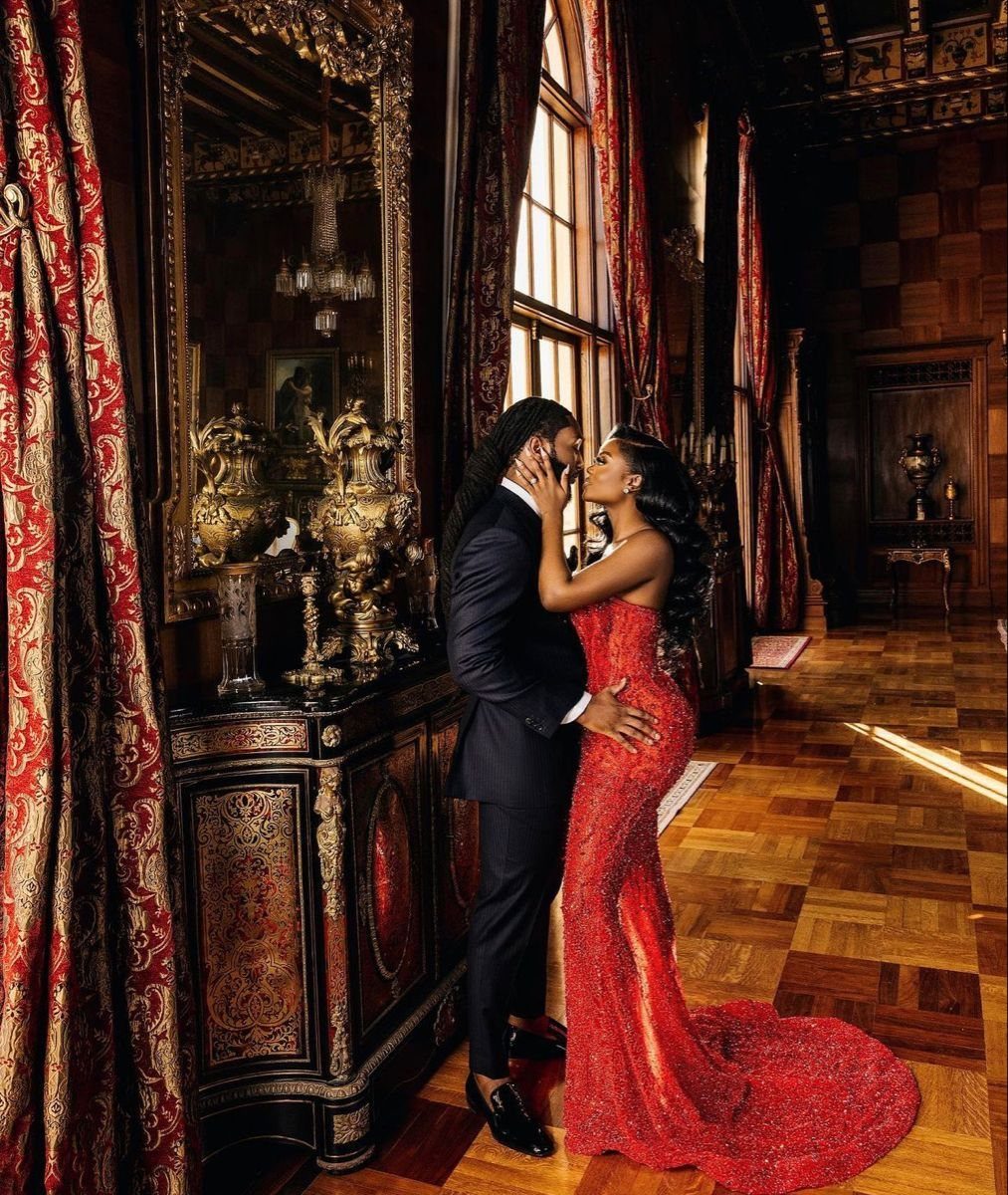 Black couple posing in an ornate room, man in black suit, woman in red sequined gown