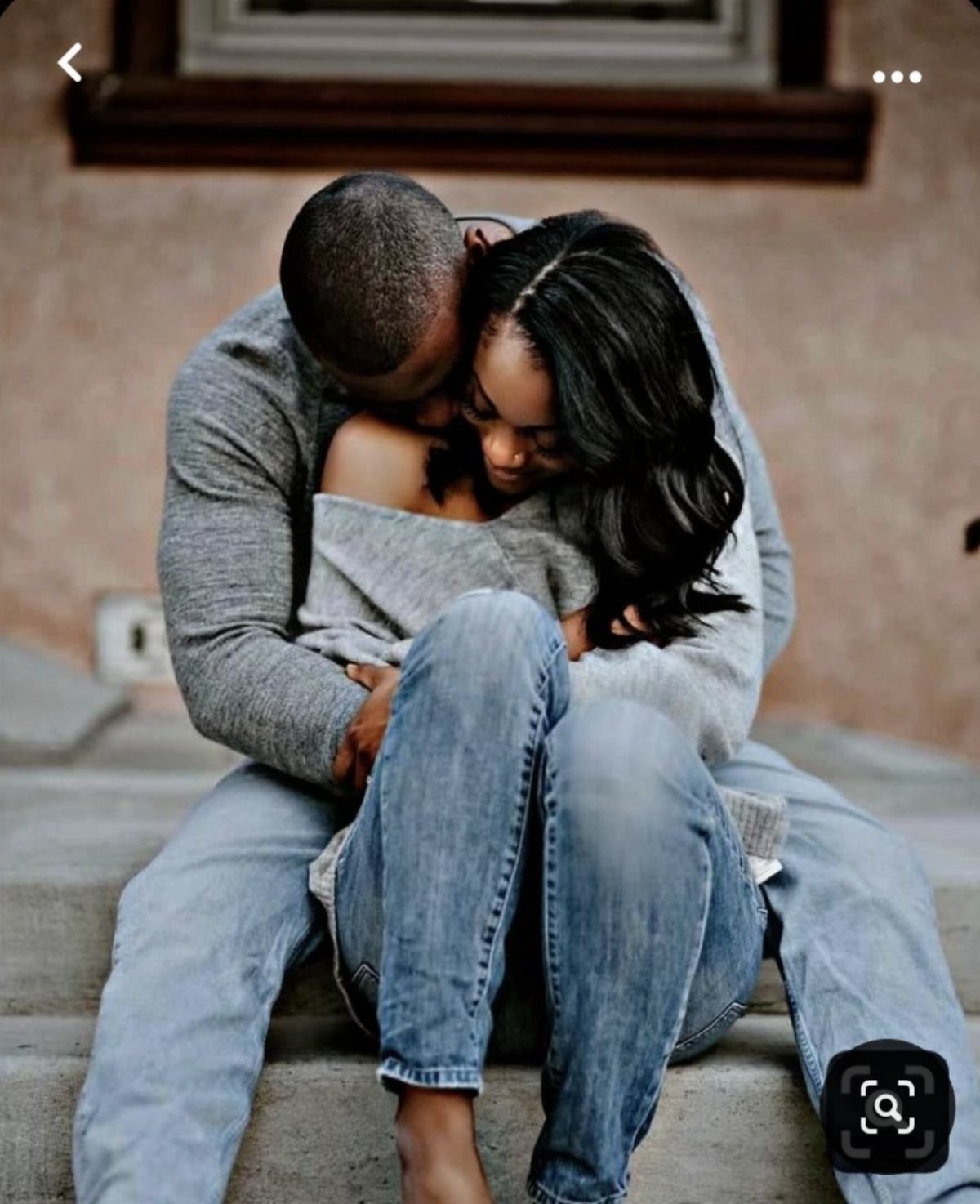 Black couple in grey knit sweaters and jeans embracing on concrete steps