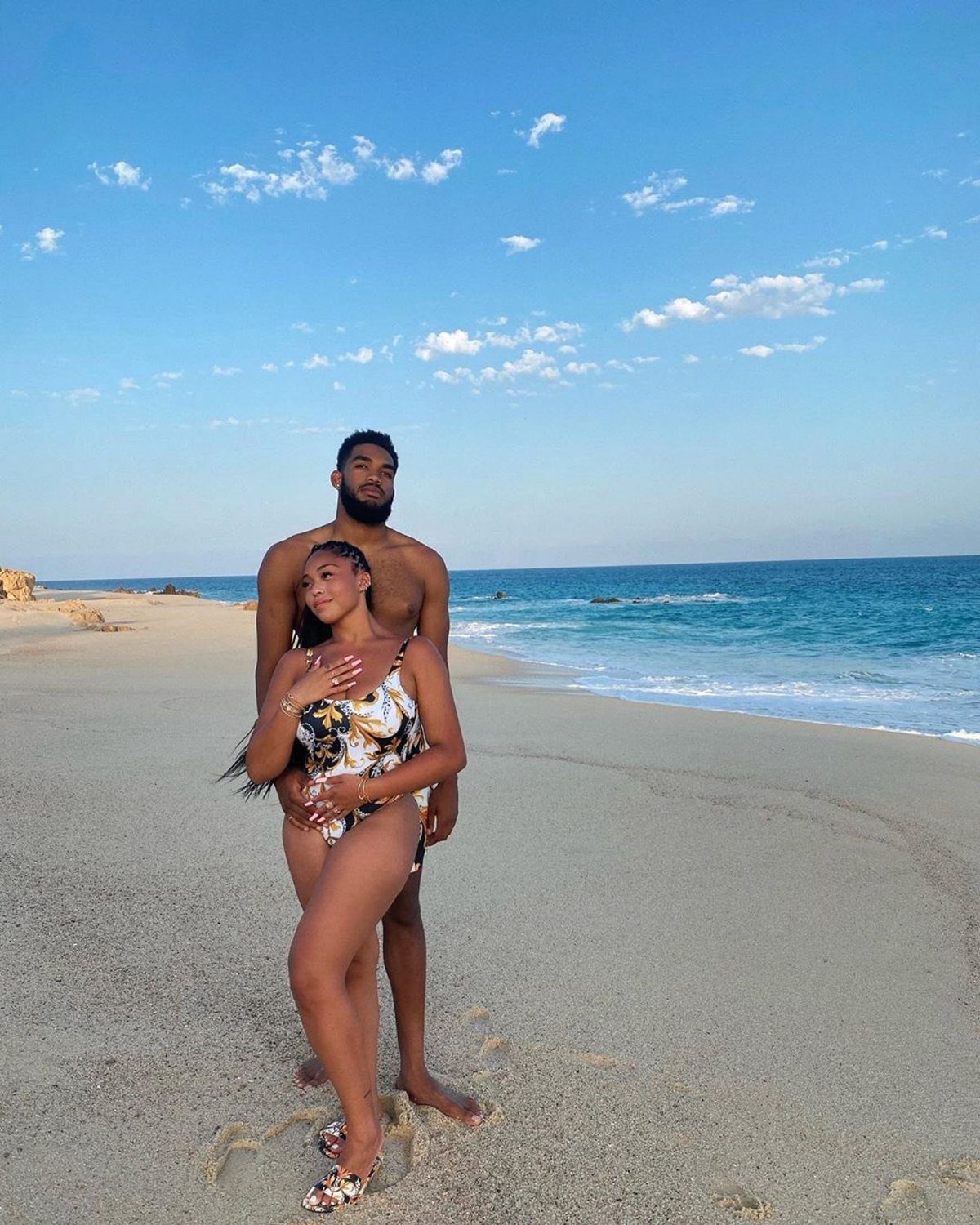 Black couple posing on a sandy beach with the blue ocean behind them.