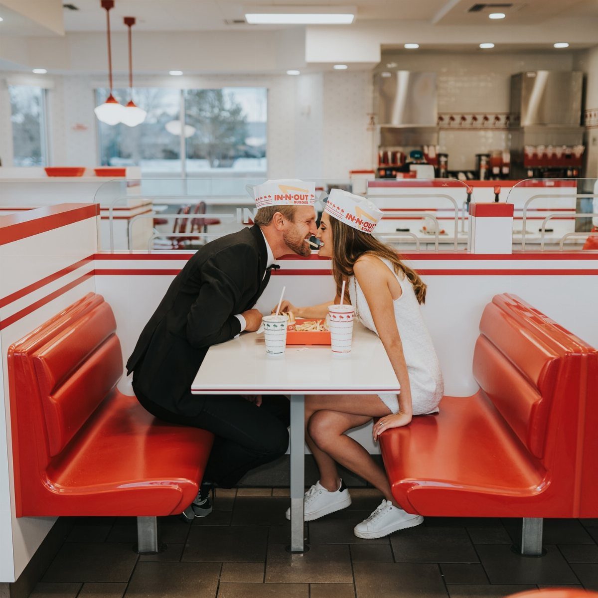 Bride and groom in fast food uniforms sharing fries in a red booth