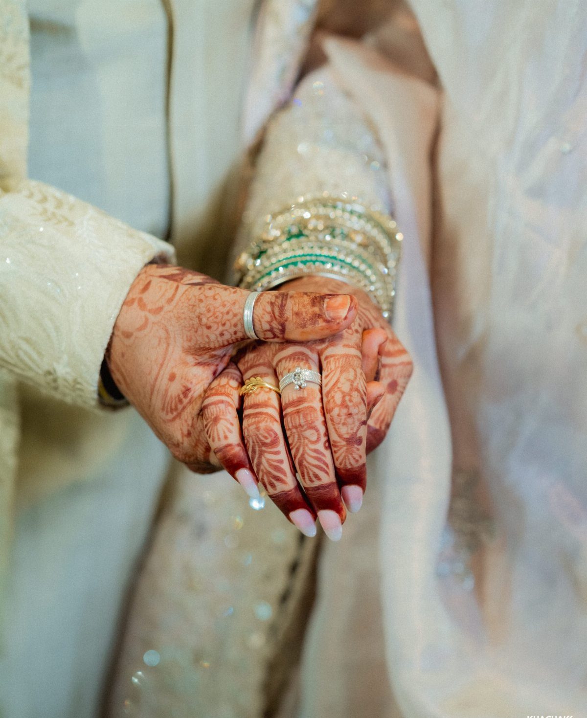 Bride and groom holding hands, featuring detailed henna and traditional wedding jewelry.