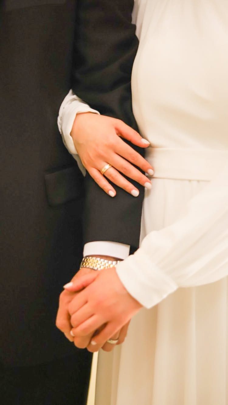 Close-up of a bride and groom holding hands, showcasing their gold wedding rings.