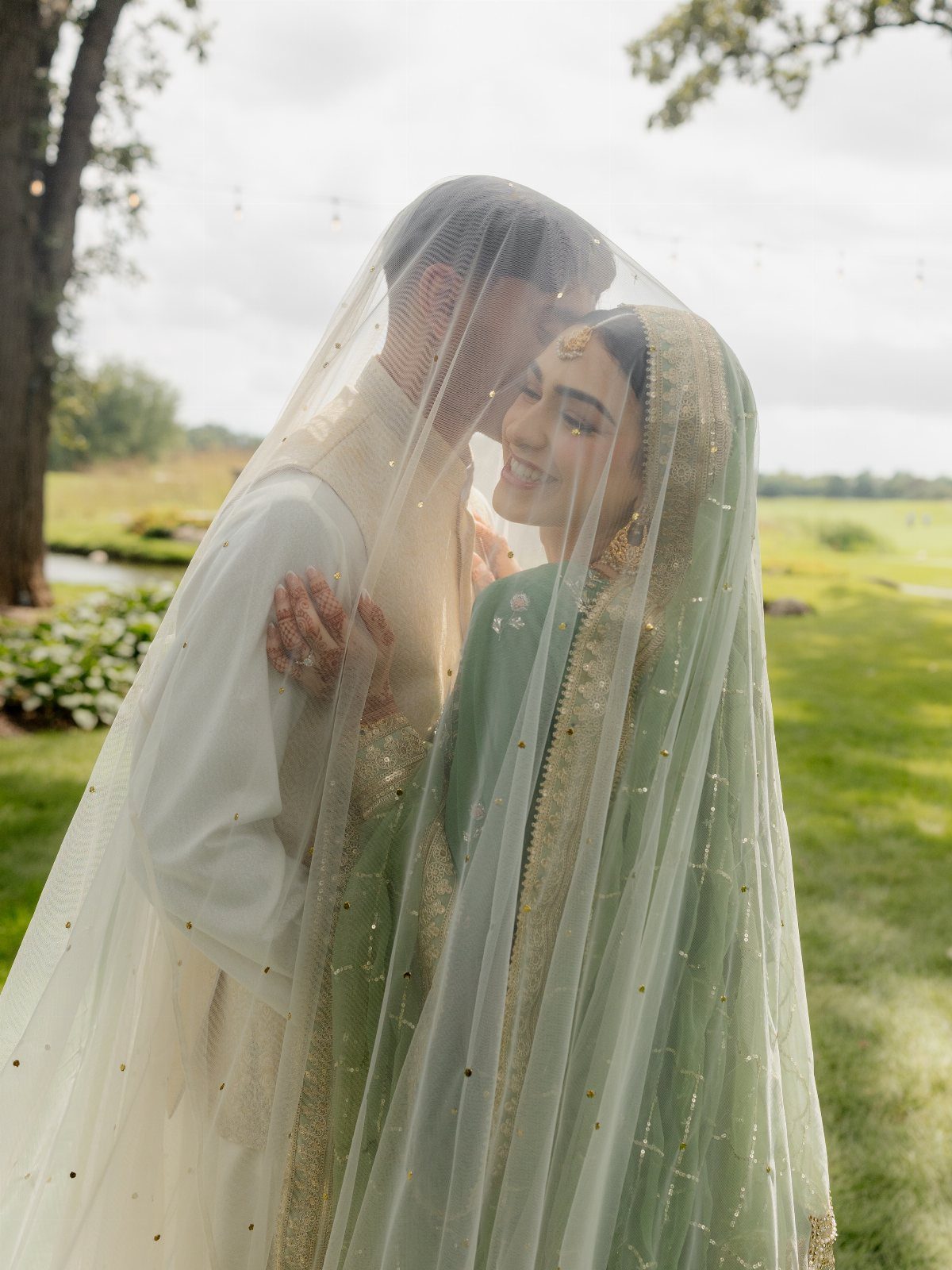 Bride and groom gazing into each other's eyes under a sheer shimmering veil.