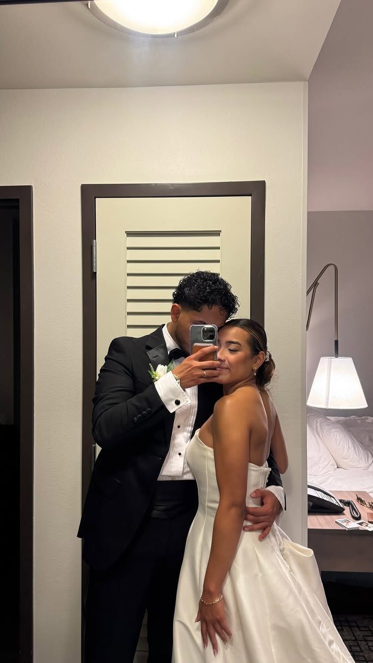 Bride and groom taking a mirror selfie while embracing in a hotel room.