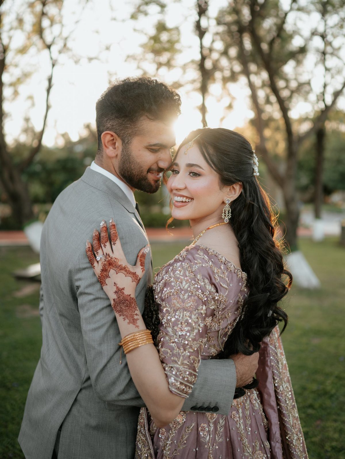 Couple in wedding attire embracing and smiling outdoors with soft sunlight behind them.