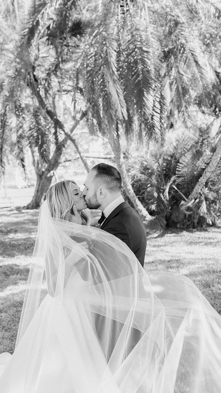 Bride and groom kissing while draped in a flowing, sheer white wedding veil.