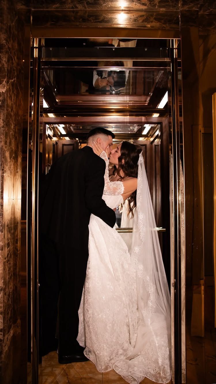 Bride and groom kissing inside a luxurious gold-framed glass elevator with mirrored ceilings.