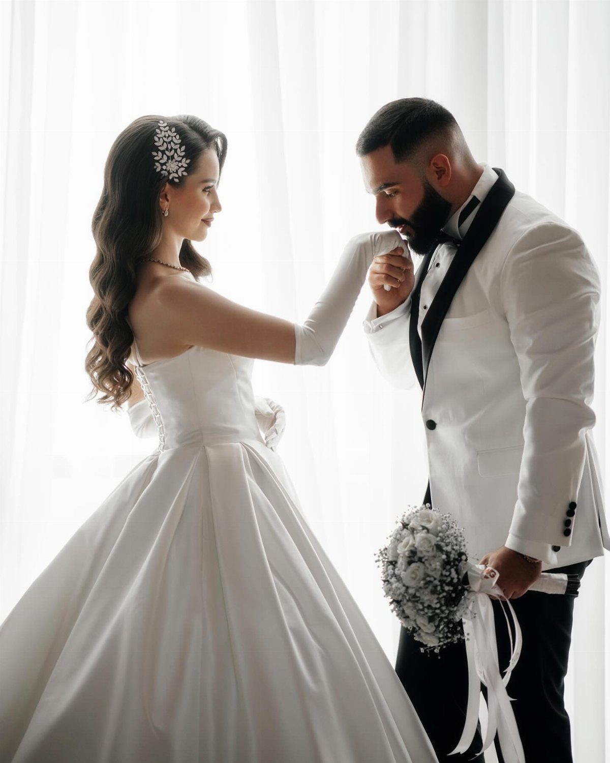 Groom in white tuxedo kissing the hand of a bride in a white gown.