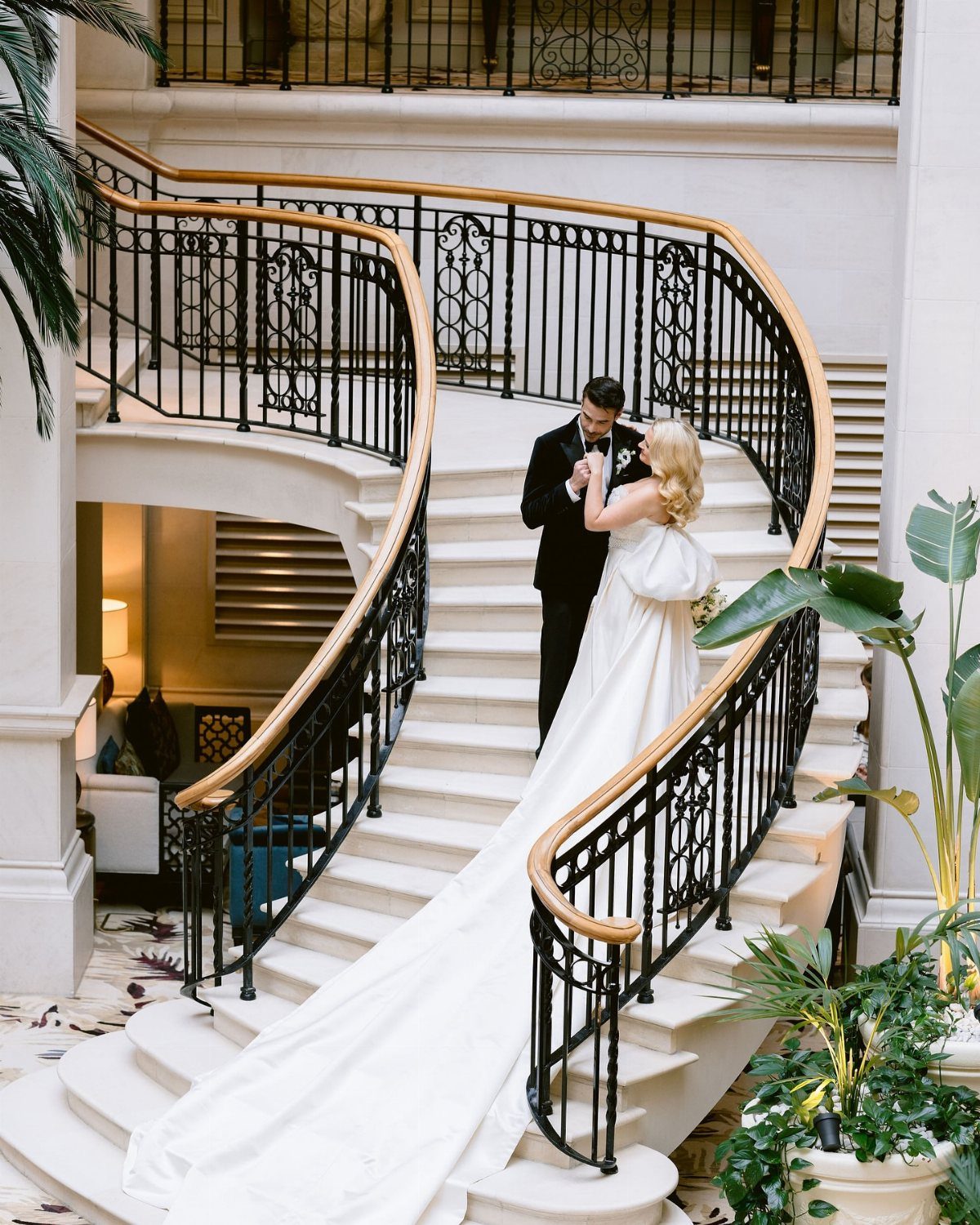 Bride and groom posing on a sweeping white staircase with black railings.