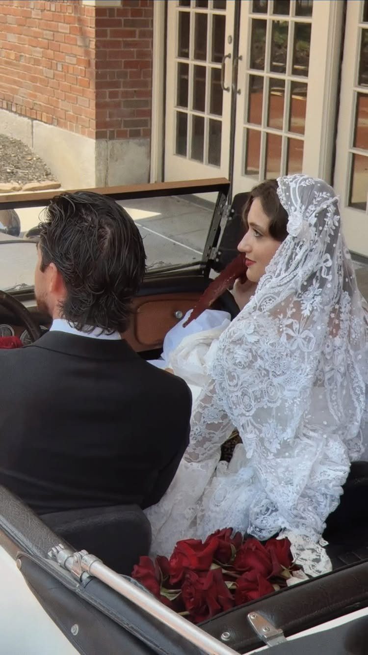 Bride and groom sitting in a vintage convertible car with red roses.