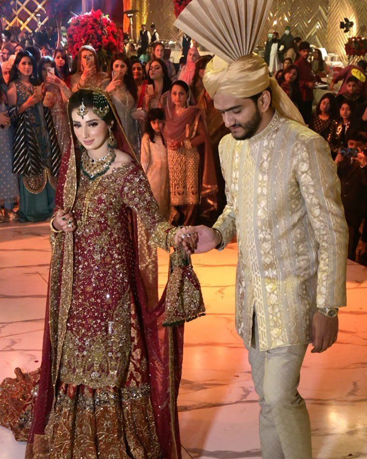 Bride and groom in traditional South Asian wedding attire walking hand in hand.
