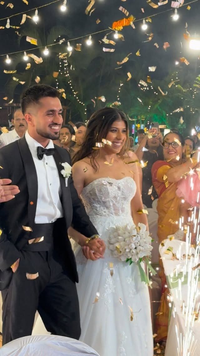 Bride and groom walking hand in hand through gold confetti during wedding exit.