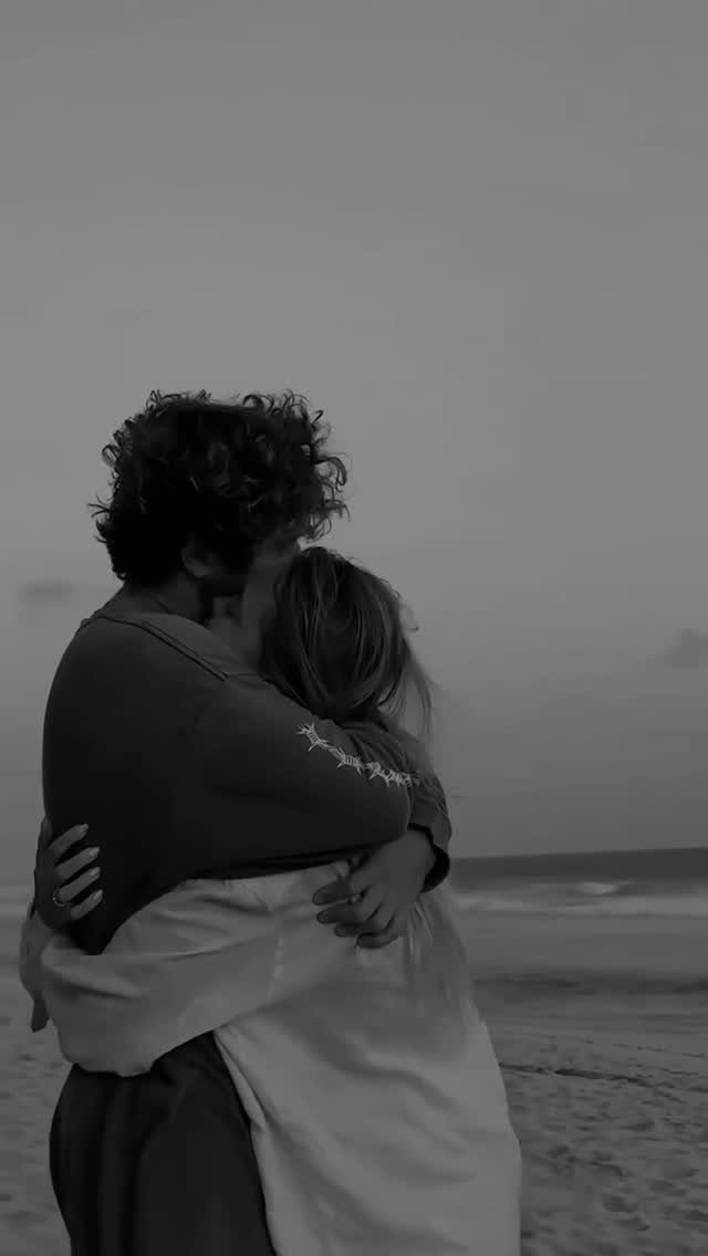 Couple embracing on a beach with the man hugging the woman from behind.