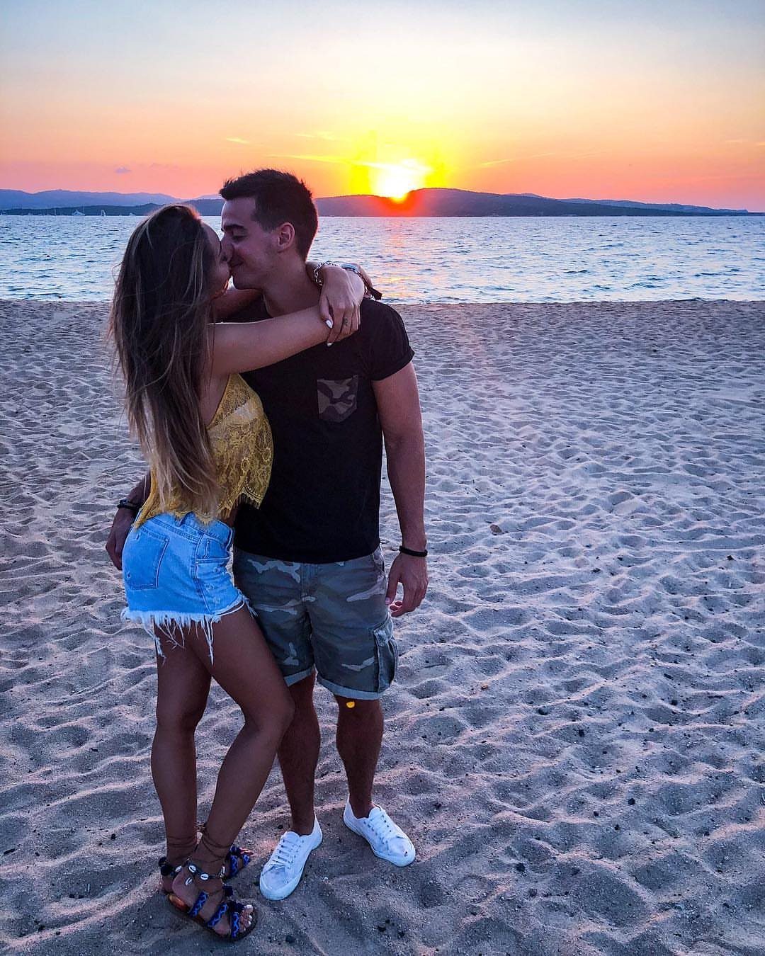 Couple kissing on a sandy beach with a bright sunset over the ocean horizon.