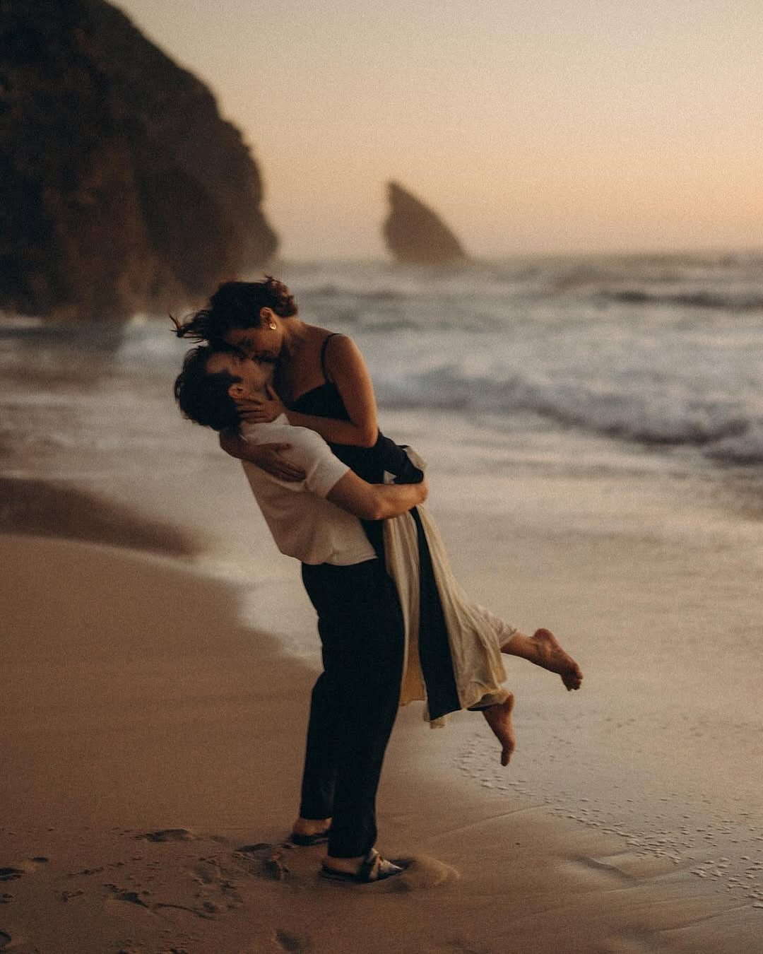 Couple embracing on a beach with the man lifting the woman up.