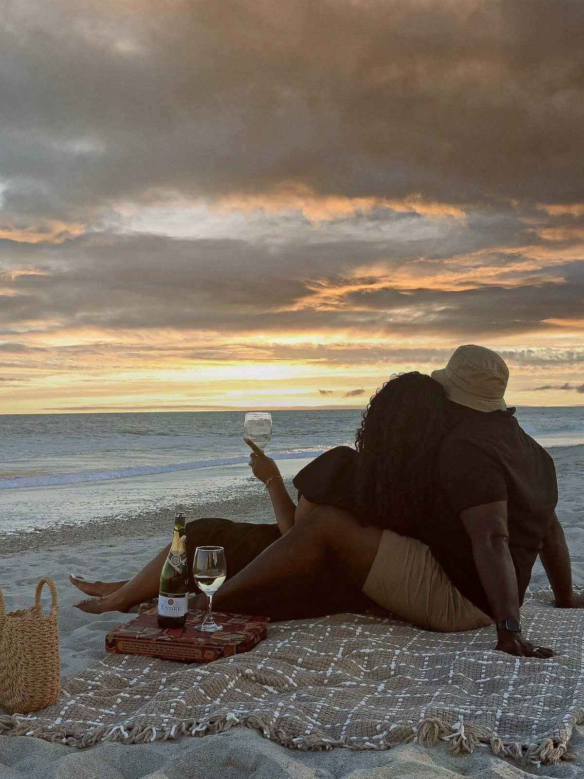 Couple sitting on a white blanket on the beach during a golden sunset.