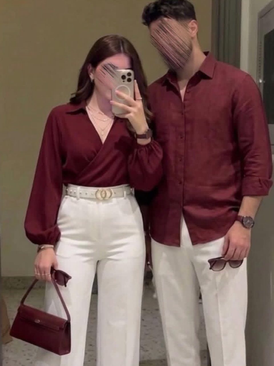 Couple wearing matching maroon shirts and white trousers posing for a mirror selfie.