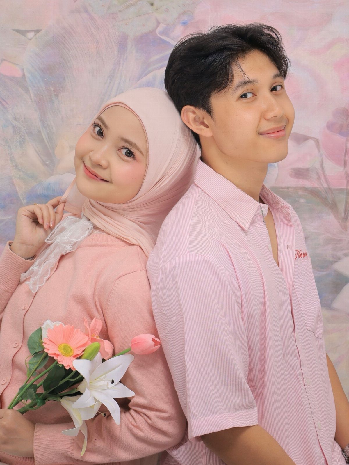 Young couple in matching pink outfits posing back-to-back with a flower bouquet.