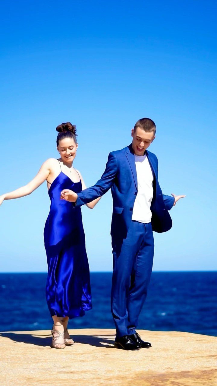 Couple in blue formal attire dancing on a cliff by the blue ocean.