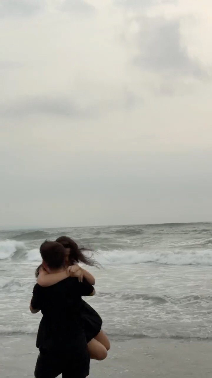 Couple embracing and hugging on a beach with ocean waves in the background.