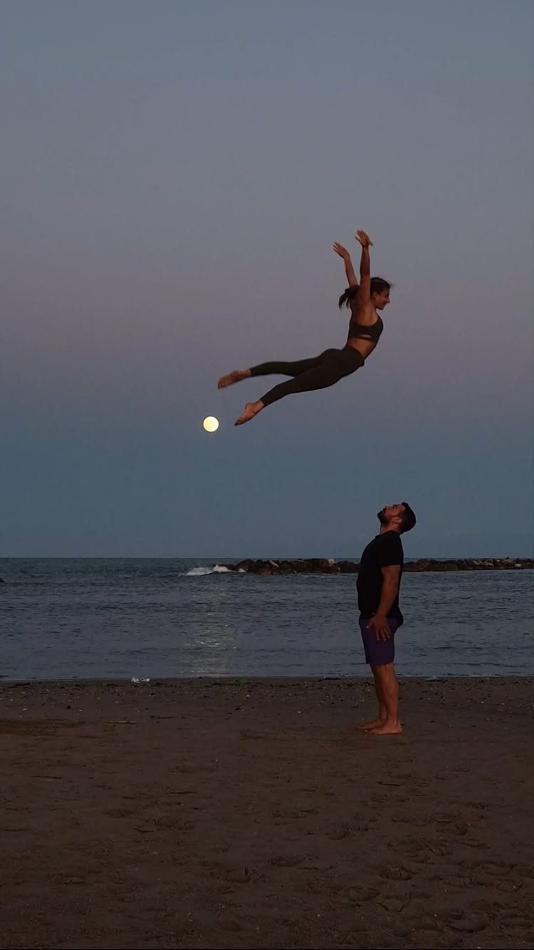Man watching a woman jump high in the air on a beach at dusk
