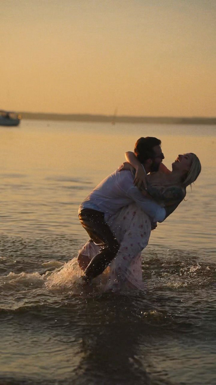 Man lifting woman in shallow ocean water during a golden sunset beach session.