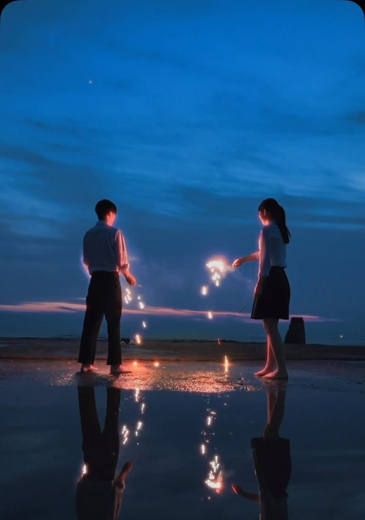 Couple holding sparklers on a beach at twilight with reflections in the water