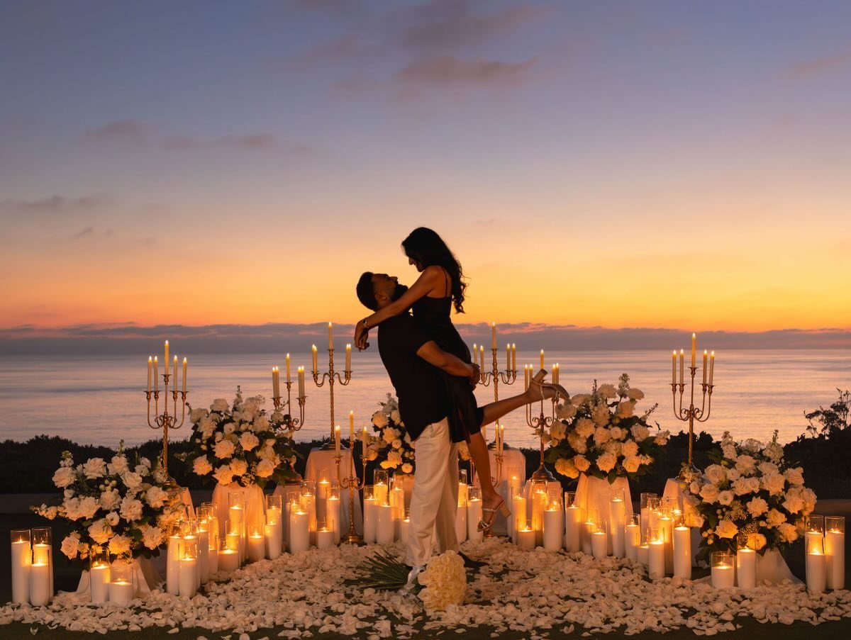 Silhouetted couple dipping during a sunset proposal surrounded by white candles and flowers.