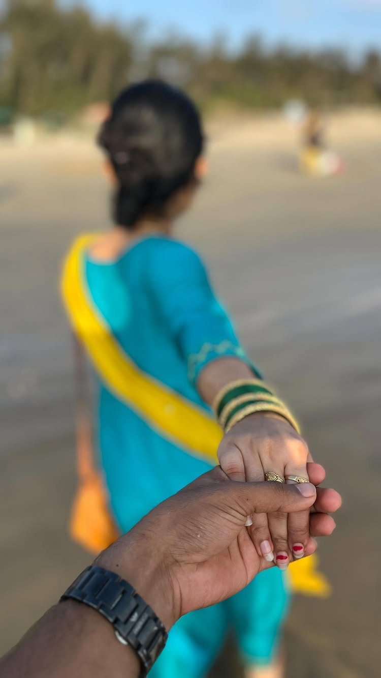 Couple holding hands on a beach with woman in blue traditional dress facing away
