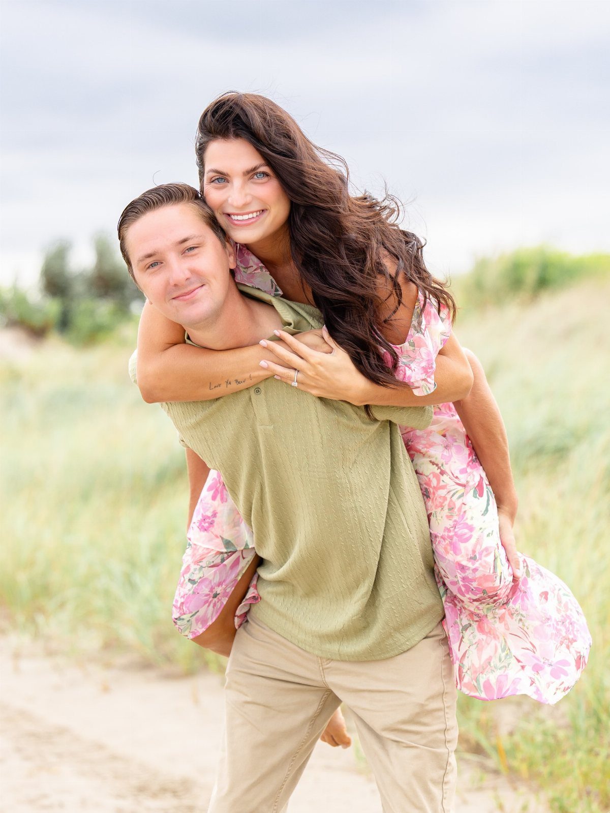 Man giving a piggyback ride to a woman in a floral dress on a beach