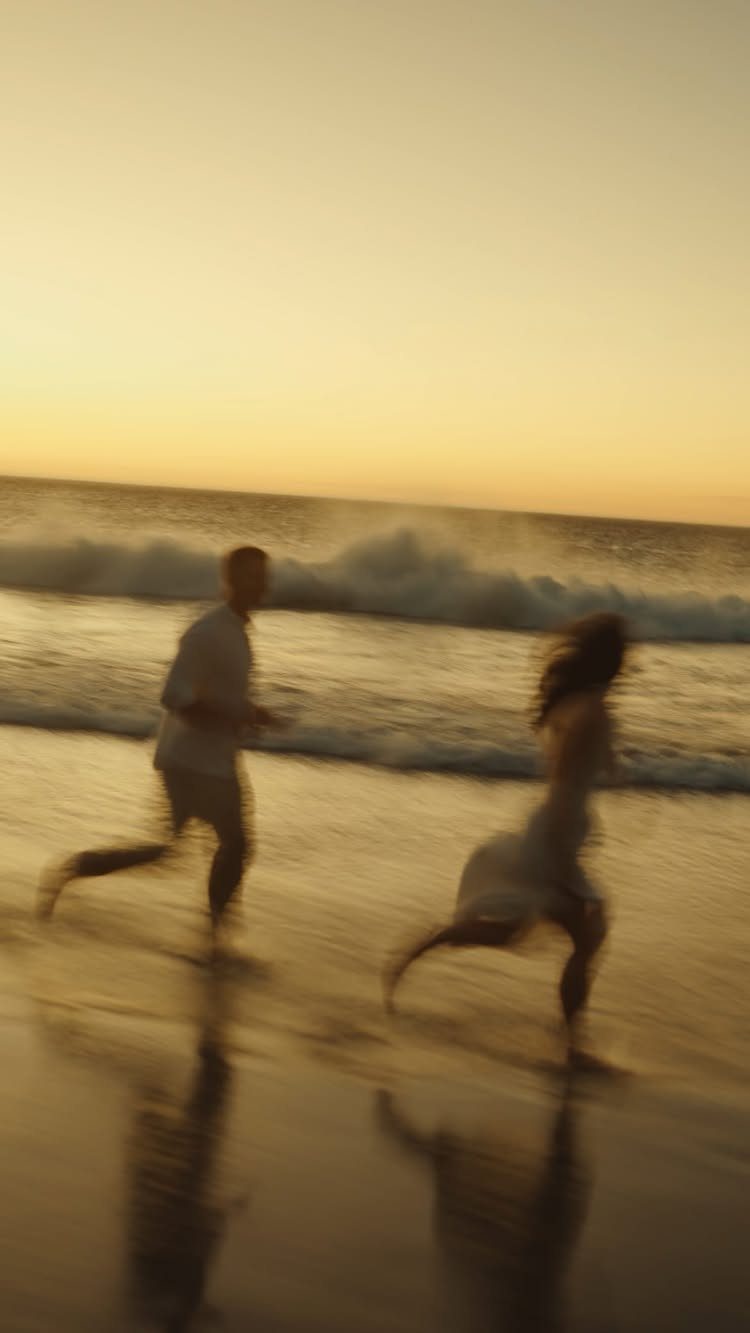 Couple running on a beach at sunset with motion blur and reflections.