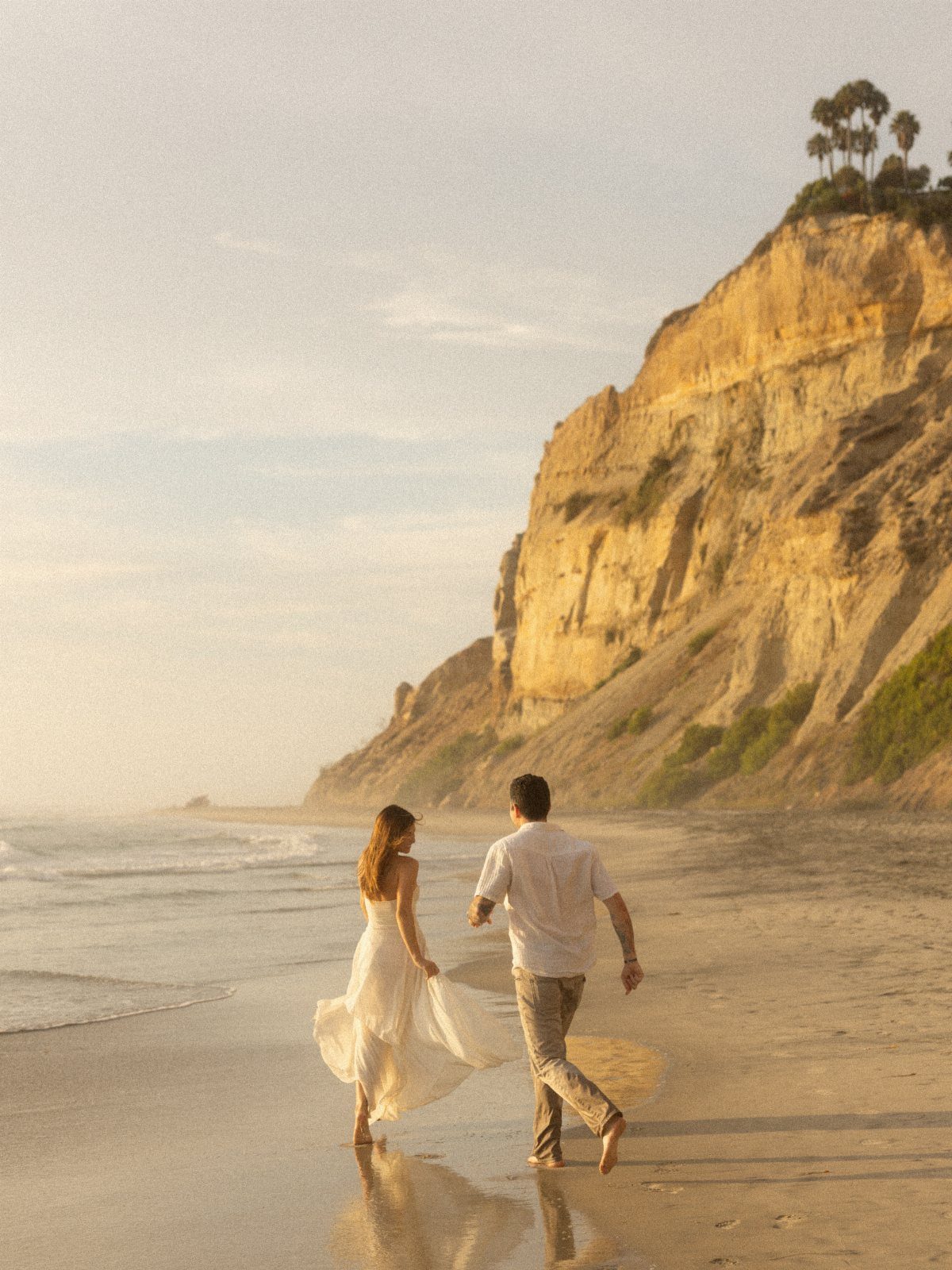 Couple walking on a sandy beach at sunset beside a golden cliffside