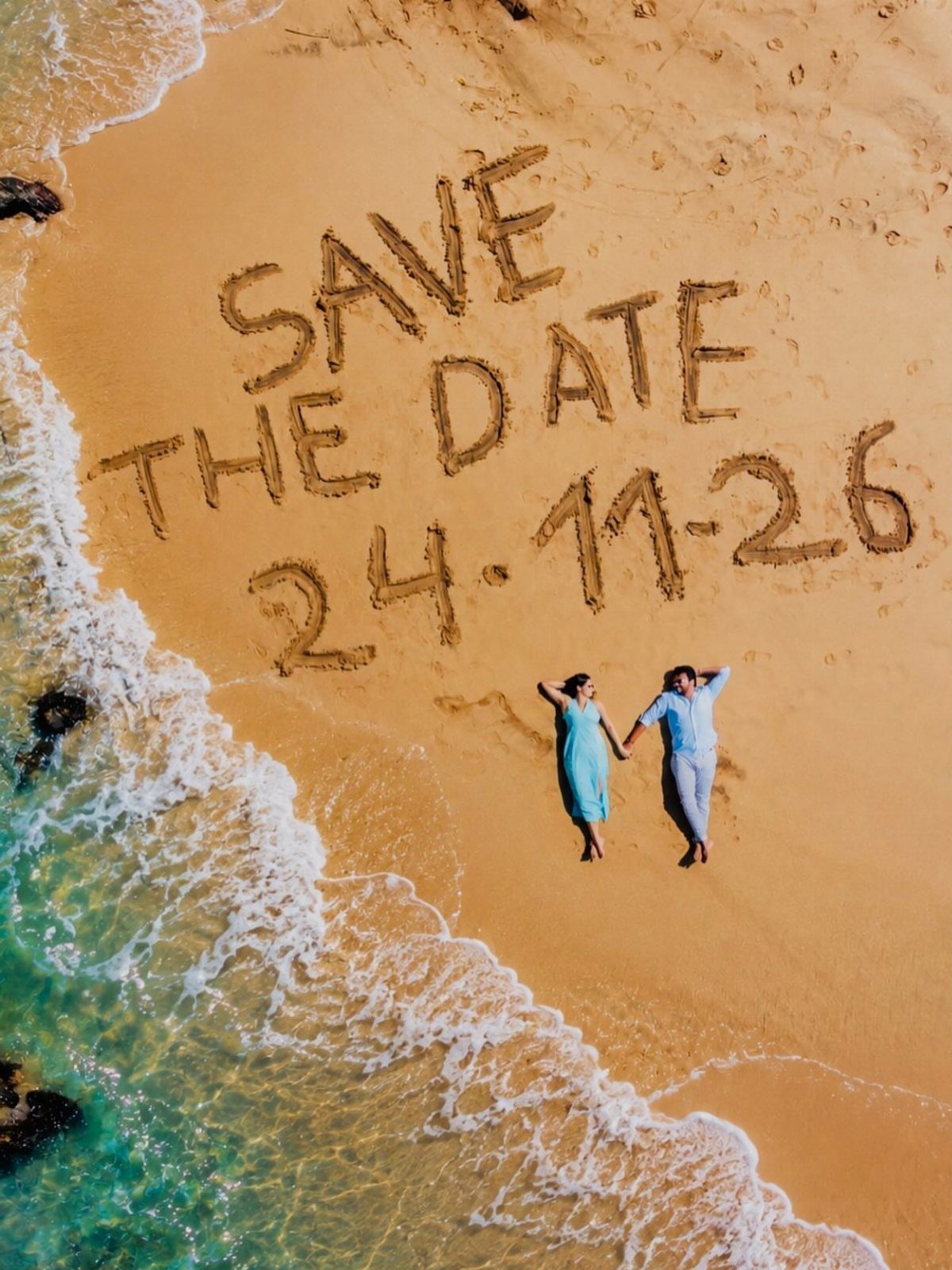 Couple lying in the sand next to a large Save the Date message.