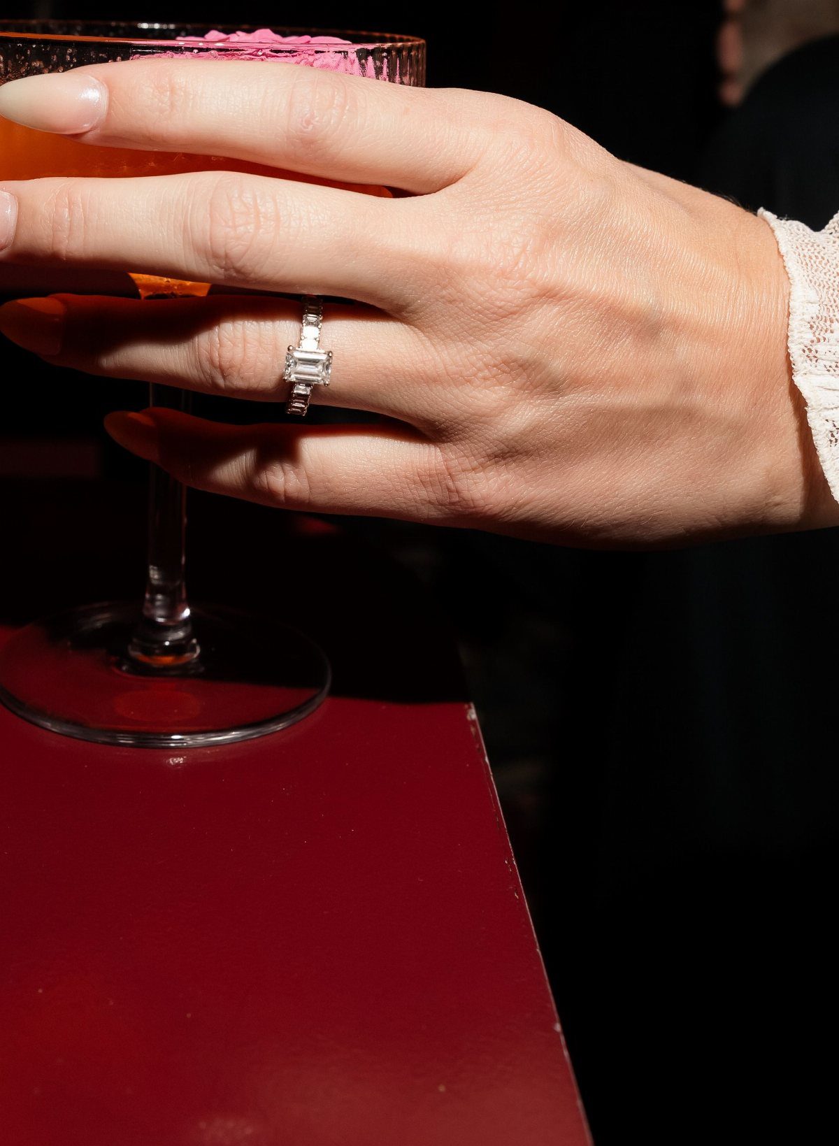 Diamond engagement ring on a hand holding a cocktail glass in a bar