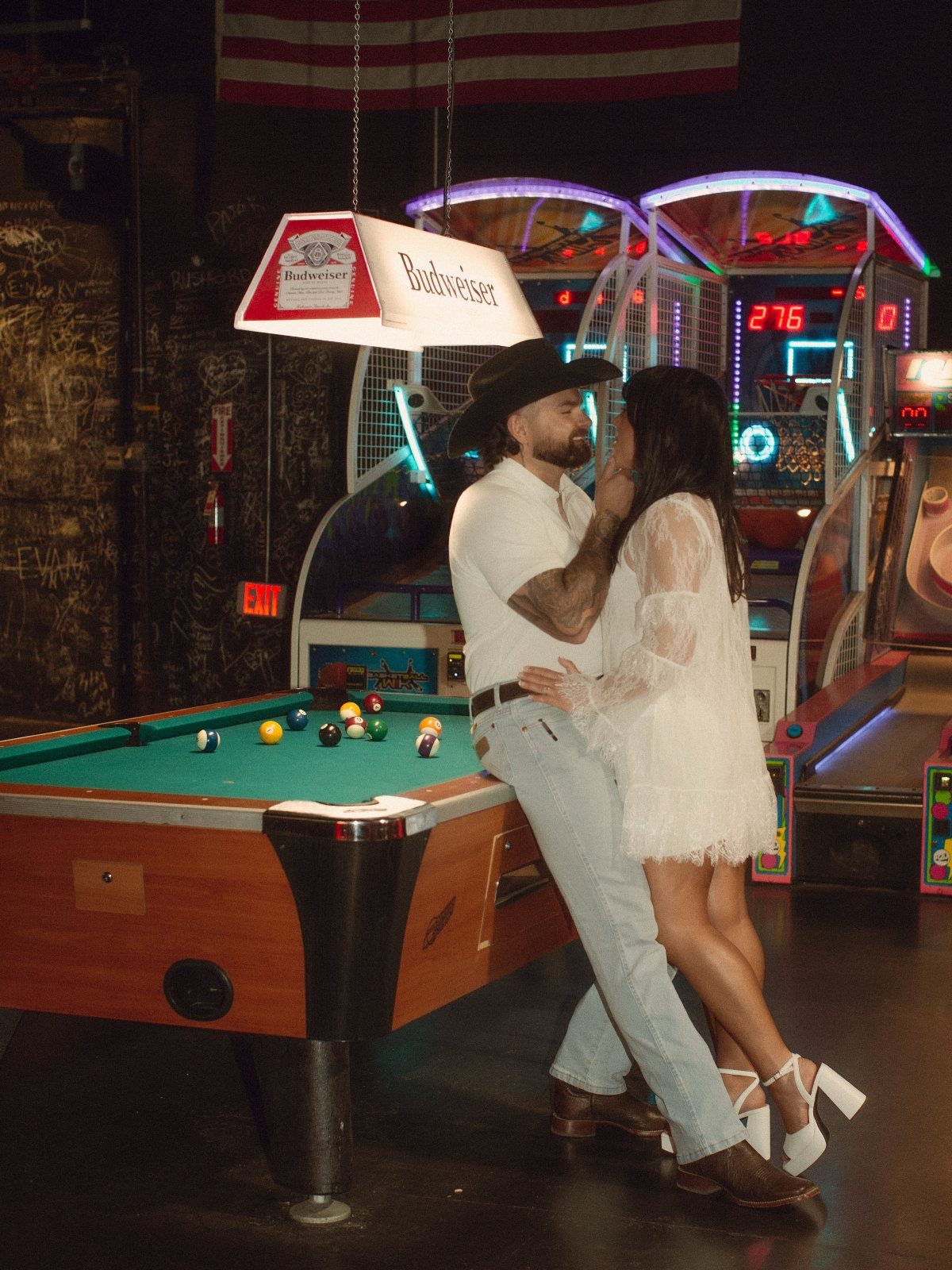Couple posing together leaning against a pool table in a dive bar setting.