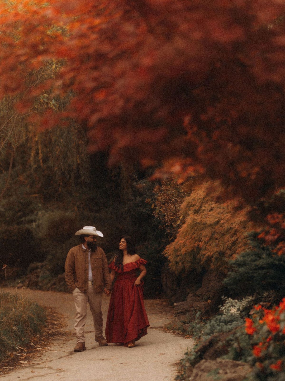 Couple walking in autumn forest, woman wearing a long burgundy dress.