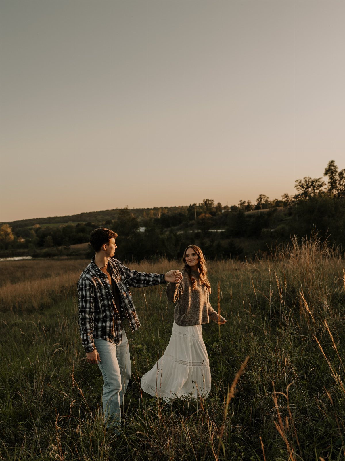 Couple in a field, man wearing a plaid flannel shirt and woman in white skirt