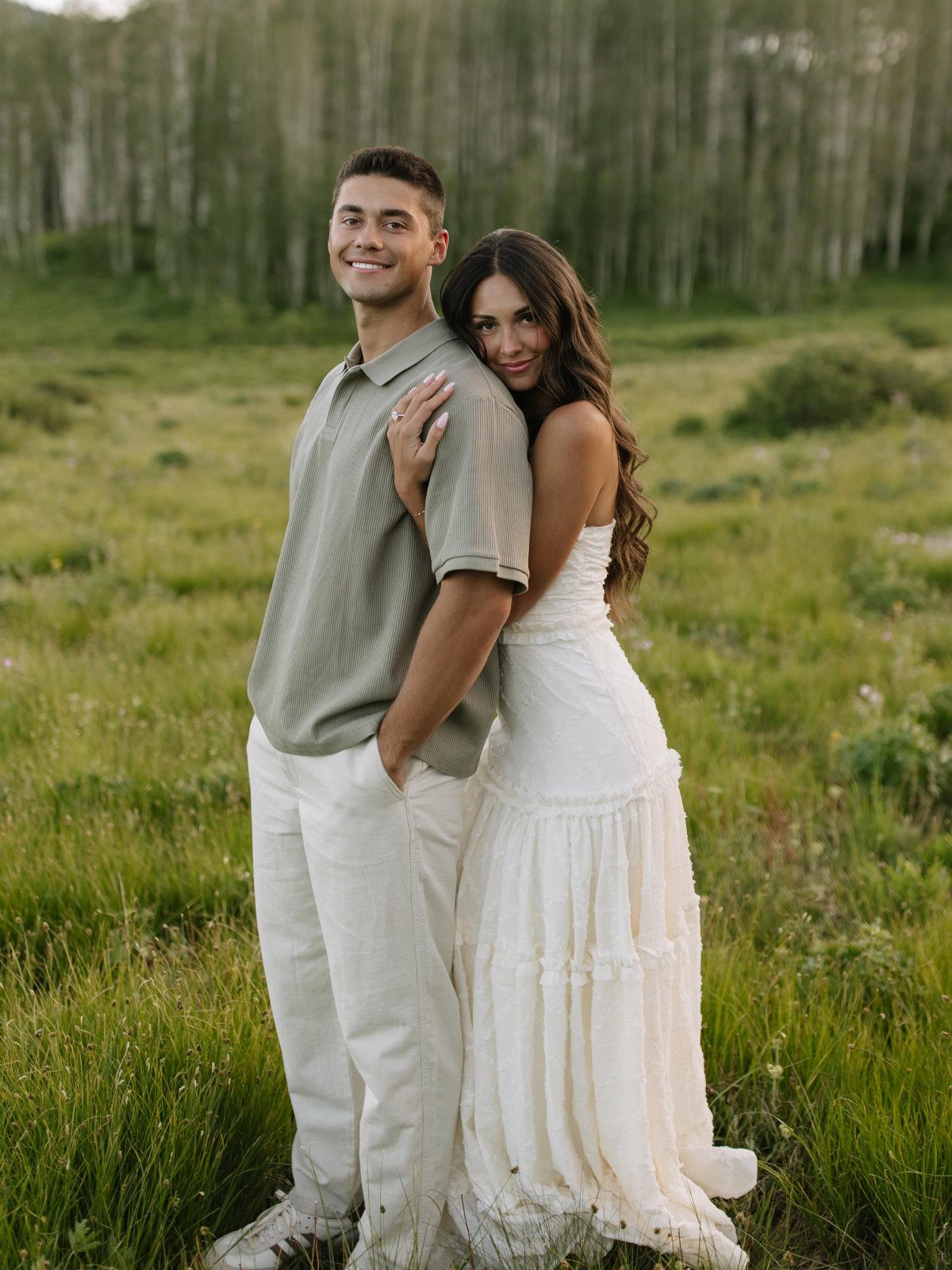 Couple posing in a field, woman wearing a long white tiered flowy dress.