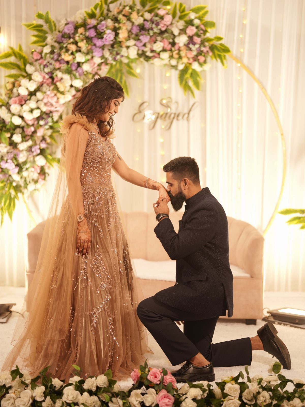 Man in dark suit kissing hand of woman in shimmering gold gown